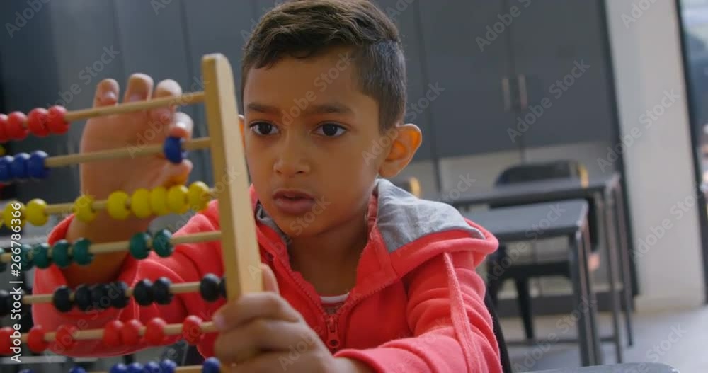 Front view of Asian schoolboy solving math problem with abacus at desk in a classroom at school 4k