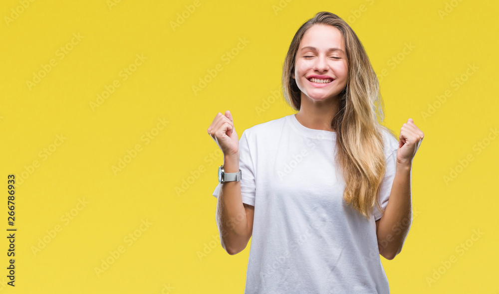 Young beautiful blonde woman wearing casual white t-shirt over isolated background excited for success with arms raised celebrating victory smiling. Winner concept. Young beautiful blonde woman wearing casual white t-shirt over isolated background excited for success with arms raised celebrating victory smiling. Winner concept.