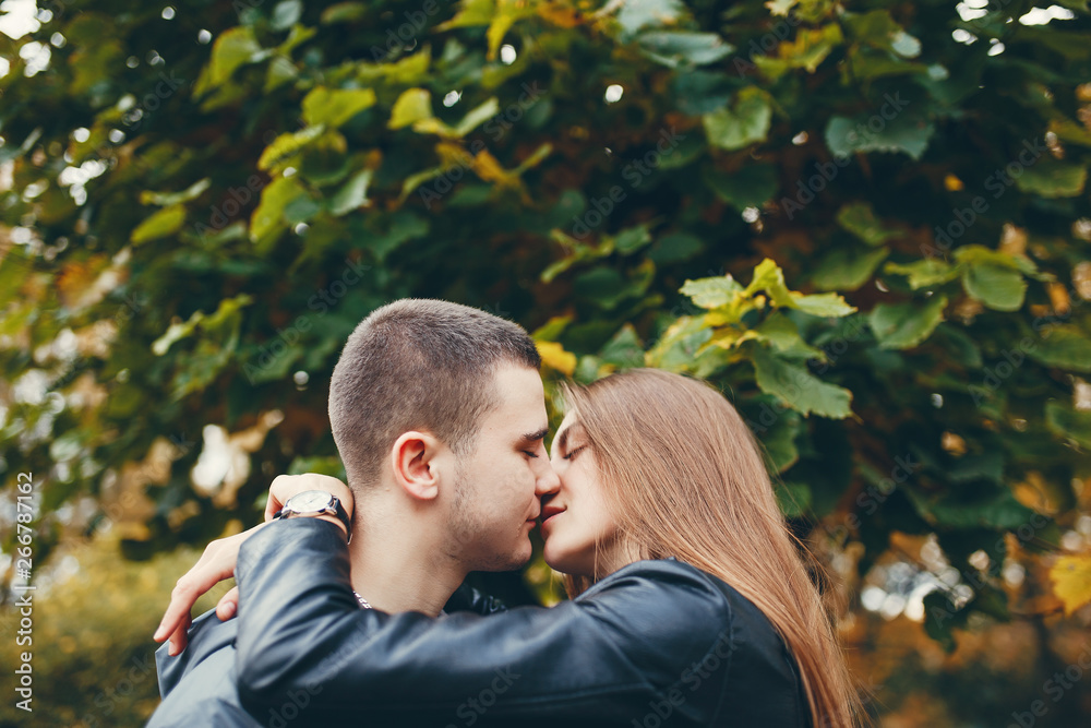 Cute couple walking in a autumn park. Boy in a black jacket. Girl in a gray dress Cute couple walking in a autumn park. Boy in a black jacket. Girl in a gray dress