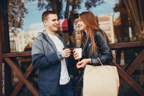 Cute couple standing near brown building. Boy and girl have fun in a autumn city. Couple drinking a coffee
