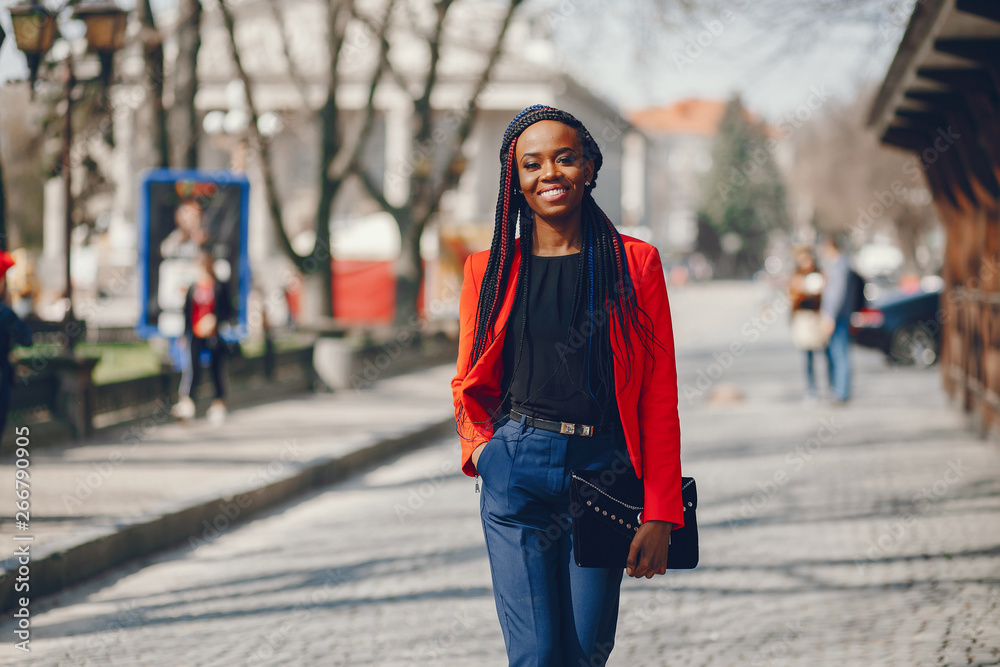 Elegant black woman standing in a summer city. Businesswoman in a red jacket