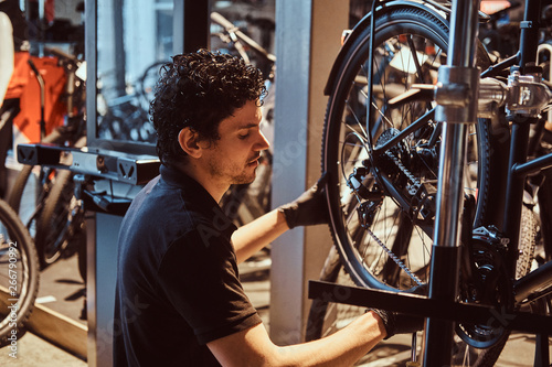 Young attractive mechanic is fixing customer's bicycle at his own workshop.