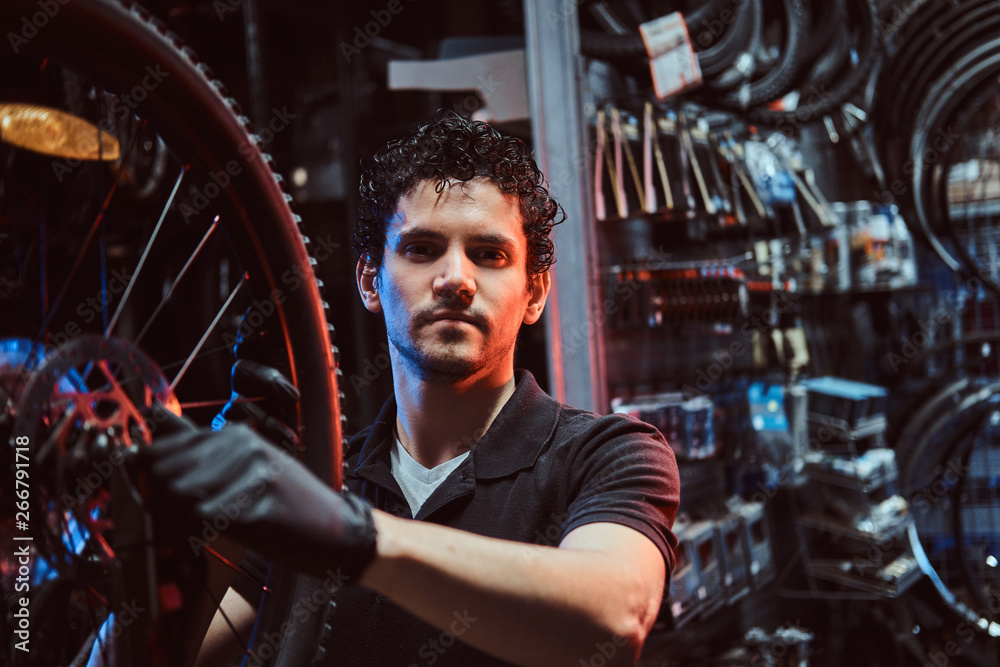Handsome diligent master is fixing bicycle's wheel at his workplace. Handsome diligent master is fixing bicycle's wheel at his workplace.