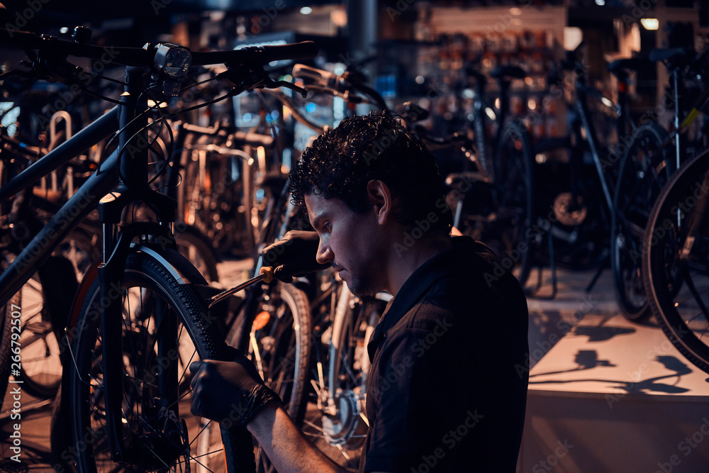 Diligent attractive mechanic is repairing customer's bicycle at workplace.