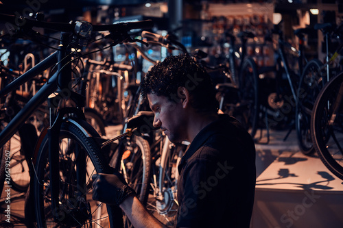 Diligent attractive mechanic is repairing customer's bicycle at workplace.