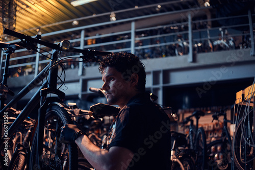 Diligent attractive mechanic is repairing customer's bicycle at workplace.