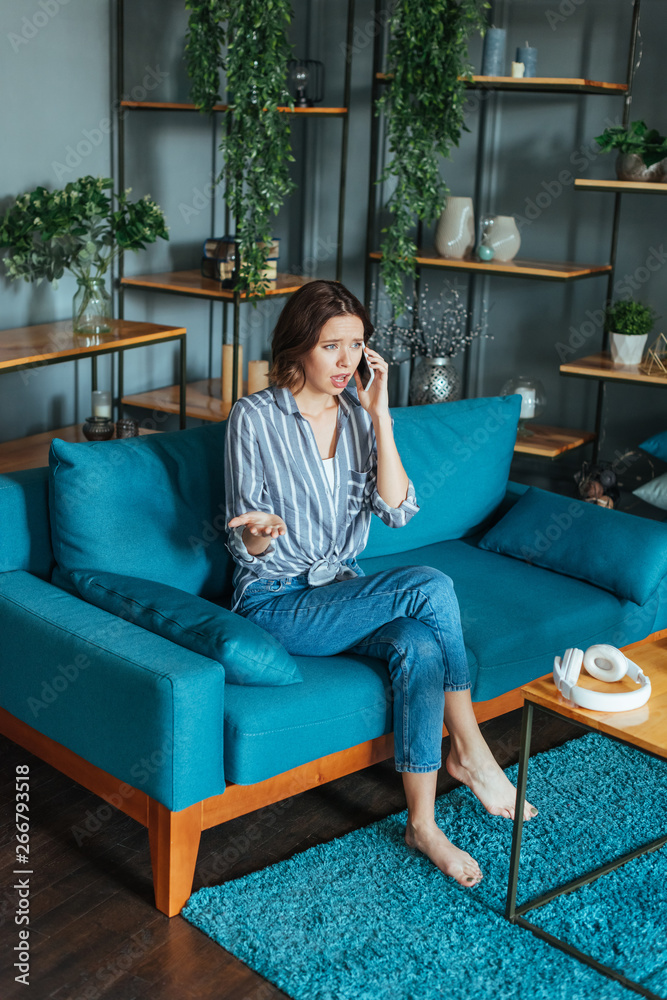 Obraz premium upset woman gesturing while talking on smartphone in living room