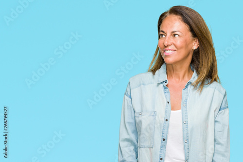 Middle age adult woman wearing casual denim shirt over isolated background looking away to side with smile on face, natural expression. Laughing confident.