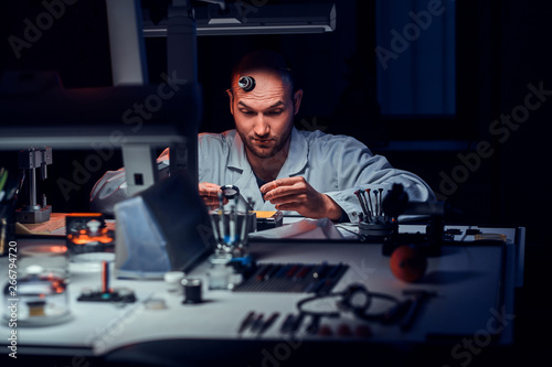 Focused man is working at his workshop with monocle and other tools repairing old watches.