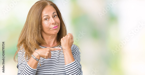 Beautiful middle age woman wearing stripes sweater over isolated background In hurry pointing to watch time, impatience, upset and angry for deadline delay