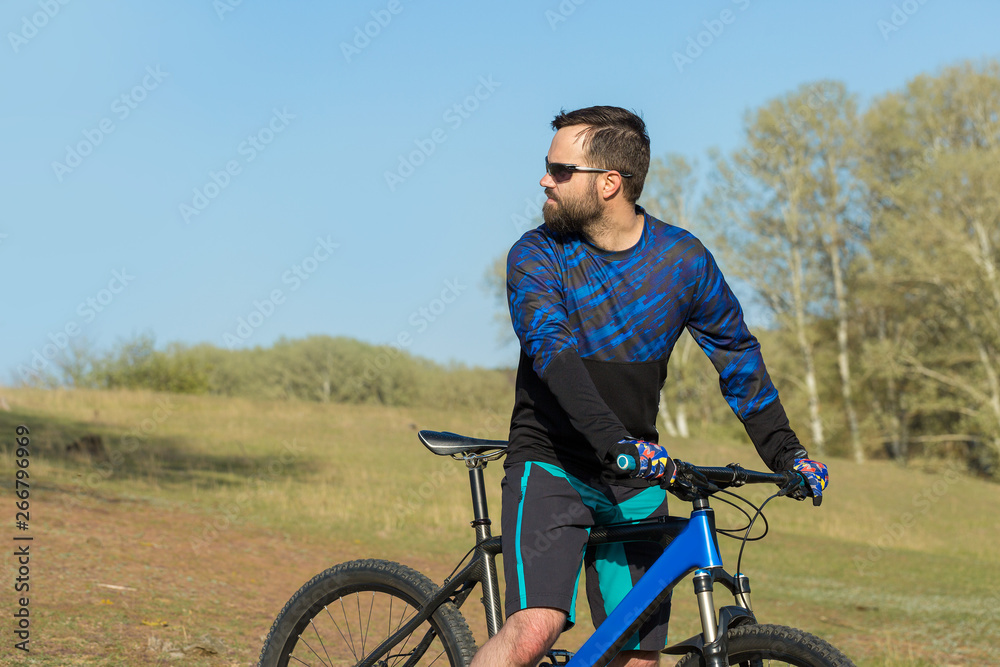 Cyclist in shorts and jersey on a modern carbon hardtail bike with an air suspension fork rides off-road on green hills near the forest Cyclist in shorts and jersey on a modern carbon hardtail bike with an air suspension fork rides off-road on green hills near the forest