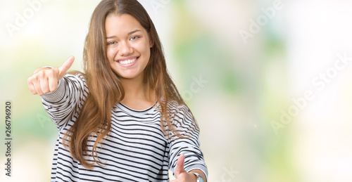 Young beautiful brunette woman wearing stripes sweater over isolated background approving doing positive gesture with hand, thumbs up smiling and happy for success. Looking at the camera