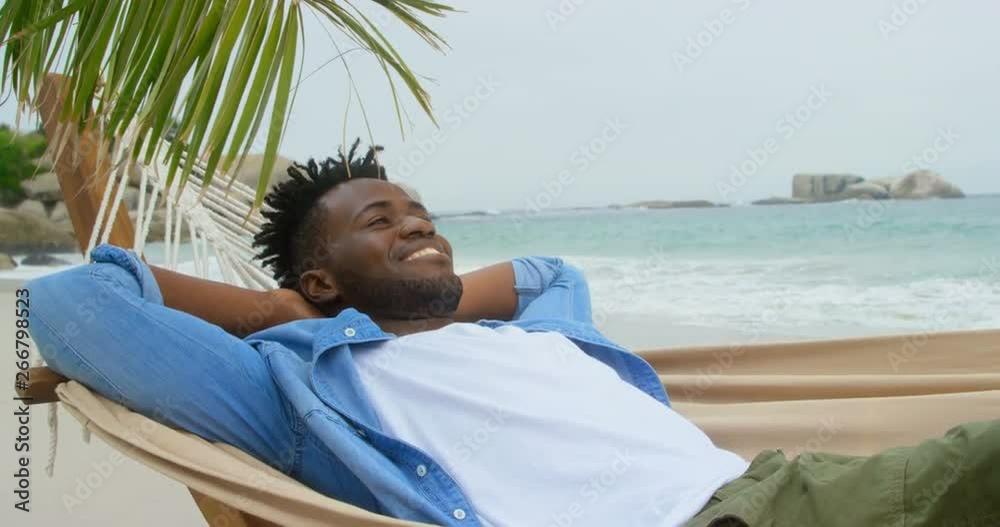 Front view of African american man relaxing in a hammock on the beach 4k