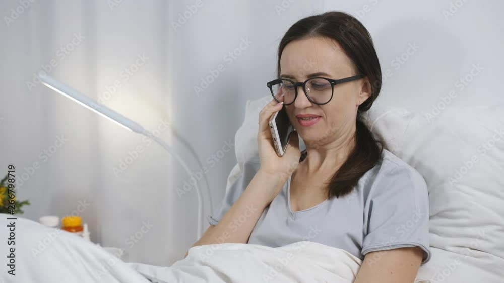 Female Patient Using Mobile Phone In Hospital Bed, close-up. Female Patient Using Mobile Phone In Hospital Bed, close-up.