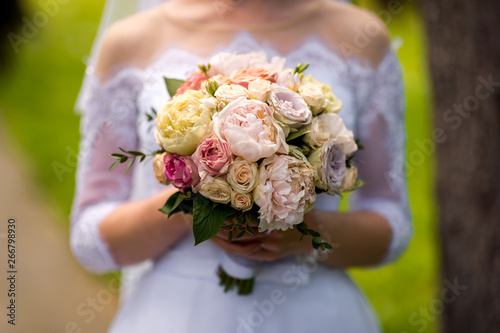 bride in a dress standing in a green garden and holding a wedding bouquet of flowers and greenery
