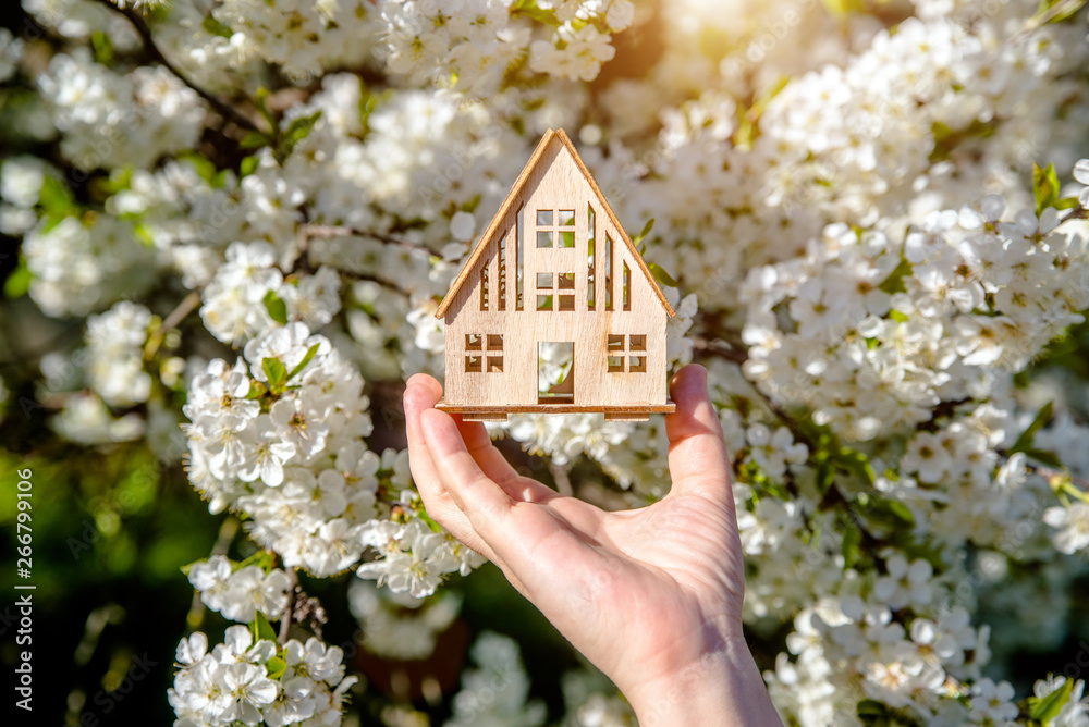 The girl holds the house symbol against the background of blossoming cherry The girl holds the house symbol against the background of blossoming cherry
