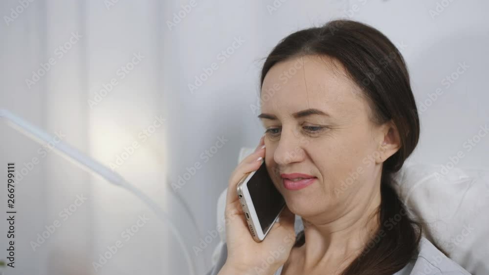 The woman in the hospital lying in bed and talking on the phone with relatives The woman in the hospital lying in bed and talking on the phone with relatives