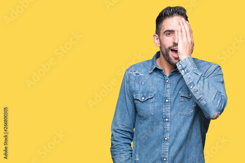 Young handsome man over isolated background covering one eye with hand with confident smile on face and surprise emotion.