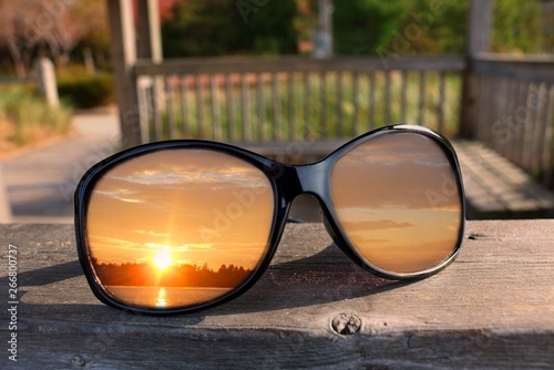 Close up of shiny black sunglasses on railing of gazebo with sunset reflecting in lenses