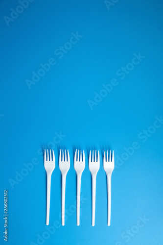 A row of lying white forks on blue background  top view. Disposable plastic tableware