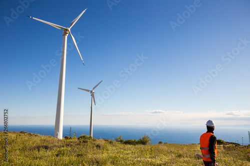 Fotografia Ingegnere elettrico controlla l'impianto eolico con il gilet ad alta visibilità e casco bianco