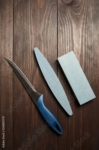 Two whetstones and steel knife, top view. Grindstones. Oval and rectangular double layer sharpening stone on wooden table background