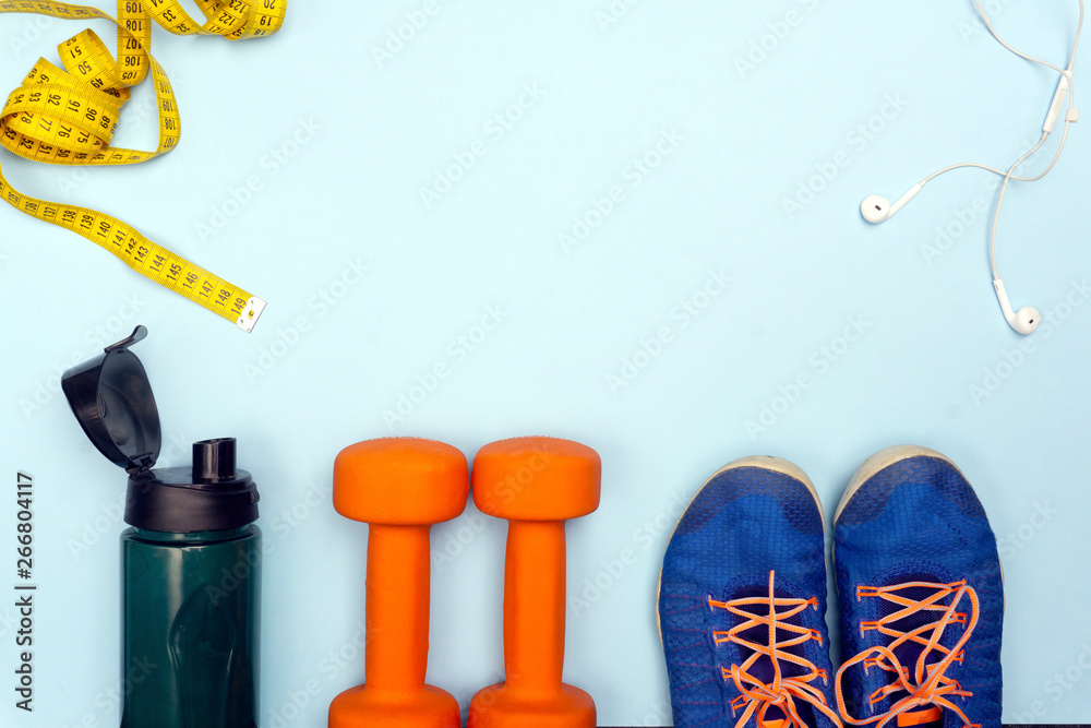 Sport concept with sport equipment composition. Sneakers, dumbbells, bottle of water on bright blue background