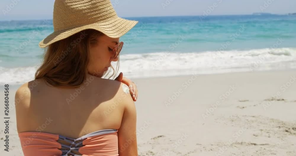 Rear view of Caucasian woman applying lotion on her body at beach 4k Rear view of Caucasian woman applying lotion on her body at beach 4k