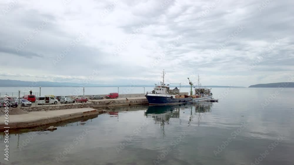 Wide, slow panning shot across Croatia harbour & medium sized fishing boat moored securely to pier. Background view of seascape & mountains under dramatic cloudy sky. Wide, slow panning shot across Croatia harbour & medium sized fishing boat moored securely to pier. Background view of seascape & mountains under dramatic cloudy sky.