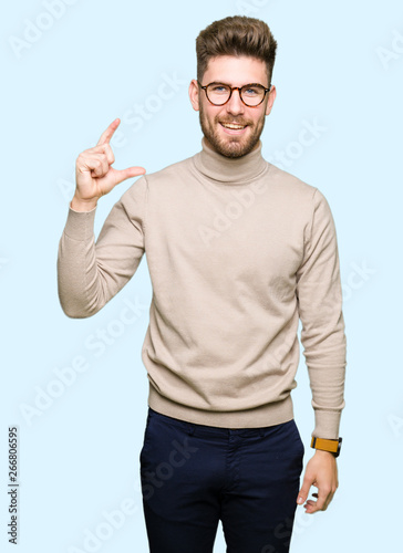 Young handsome business man wearing glasses smiling and confident gesturing with hand doing size sign with fingers while looking and the camera. Measure concept.