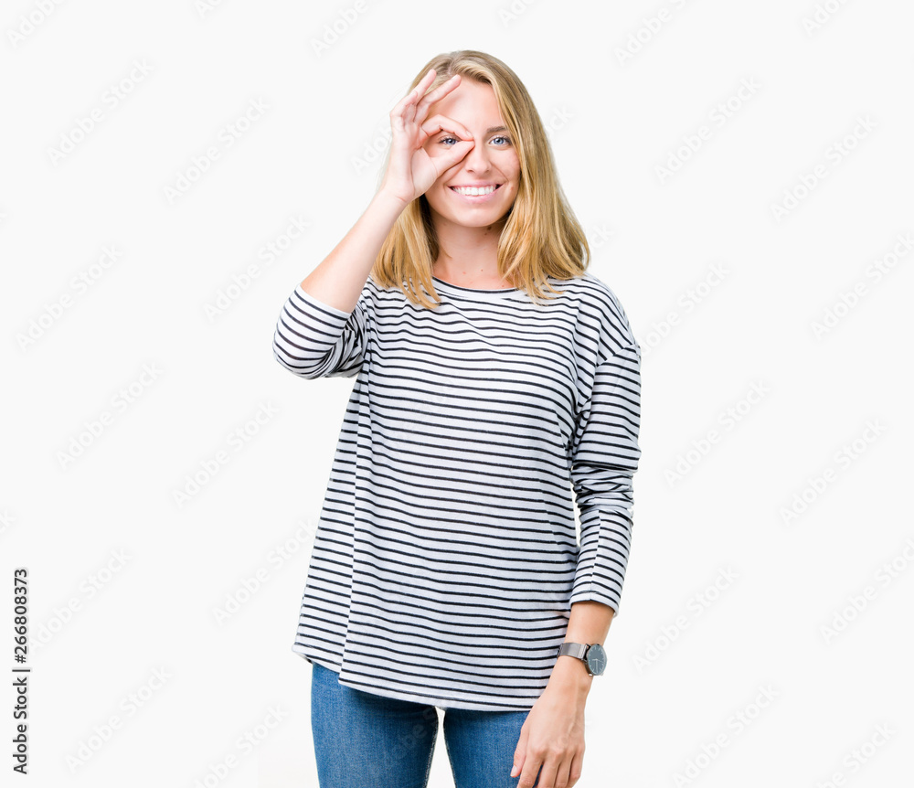 Fototapeta premium Beautiful young woman wearing stripes sweater over isolated background doing ok gesture with hand smiling, eye looking through fingers with happy face.