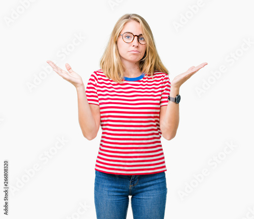 Beautiful young woman wearing glasses over isolated background clueless and confused expression with arms and hands raised. Doubt concept.