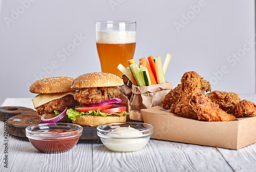 deep-fried chicken in a crafting container with two hamburgers, french fries, beer glass, vegetable sticks, sauces