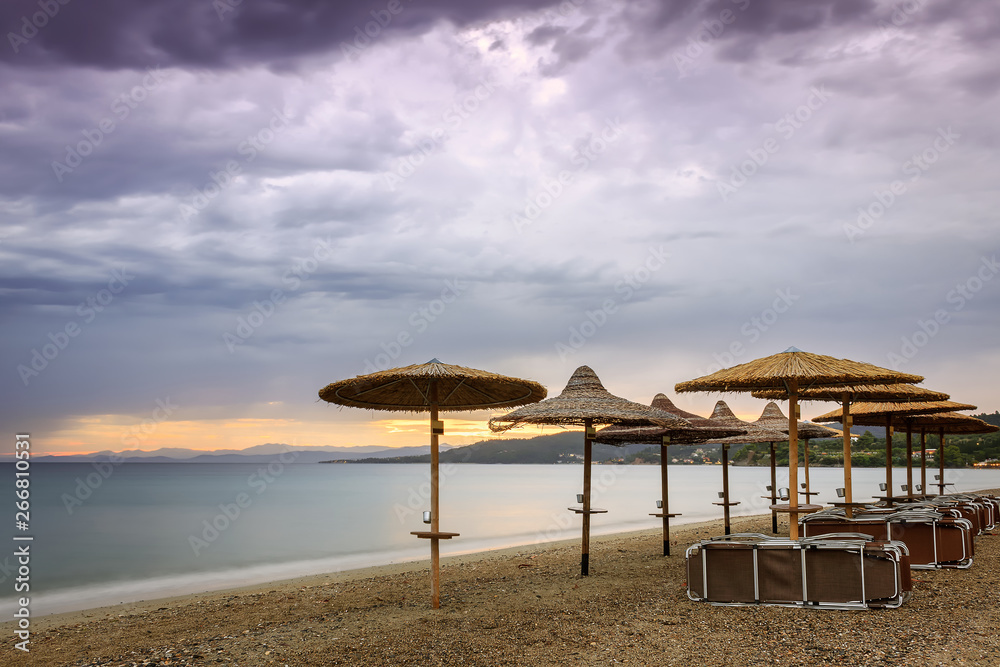 Straw beach parasol, beach beds, purple sunset sky and silky, sea water