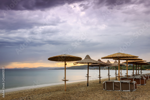 Straw beach parasol  beach beds  purple sunset sky and silky  sea water