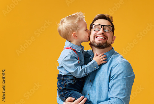 happy father's day! cute dad and son hugging on yellow background.