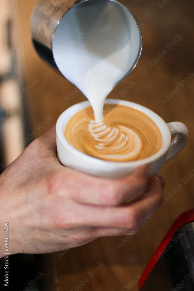 Fototapeta barista człowiek przygotowuje kawę (cappuccino), wlewając mleko
