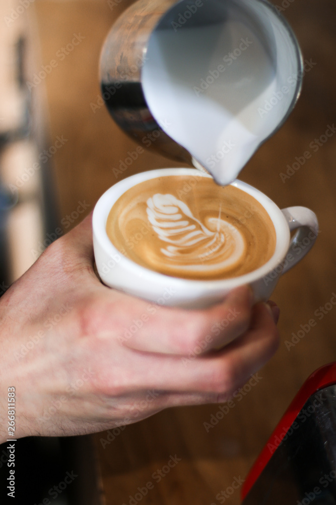 Fototapeta barista człowiek przygotowuje kawę (cappuccino), wlewając mleko