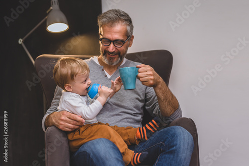 granddad and his grandson sitting on sofa and drinking coffee or tea photo