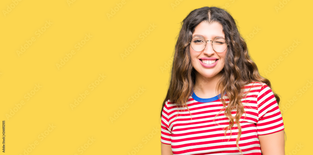 Young beautiful woman wearing glasses winking looking at the camera with sexy expression, cheerful and happy face.
