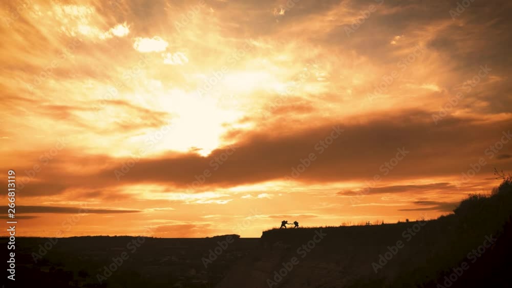 Silhouette of the team on the peak of mountain. Sport and active life of people man and girl. Teamwork couple assistance man and woman hiker, help each other on top of mountain. Silhouette of the team on the peak of mountain. Sport and active life of people man and girl. Teamwork couple assistance man and woman hiker, help each other on top of mountain.
