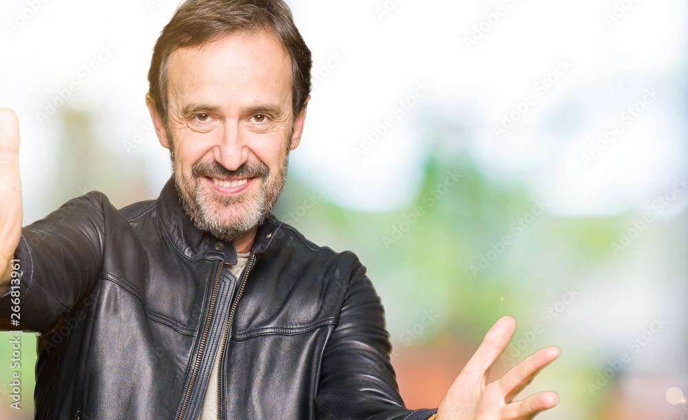 Fototapeta premium Middle age handsome man wearing black leather jacket looking at the camera smiling with open arms for hug. Cheerful expression embracing happiness.