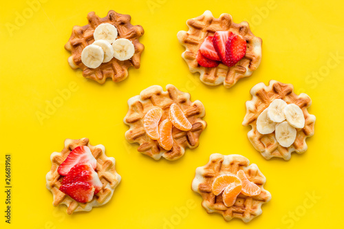 homemade Belgian waffles with fruit topings on yellow background top view