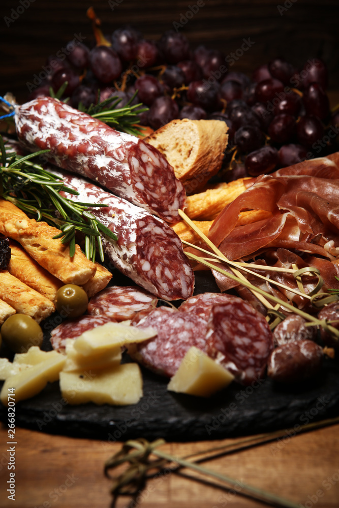 antipasto various appetizer. Cutting board with prosciutto, salami, cheese, bread and olives on dark wooden background