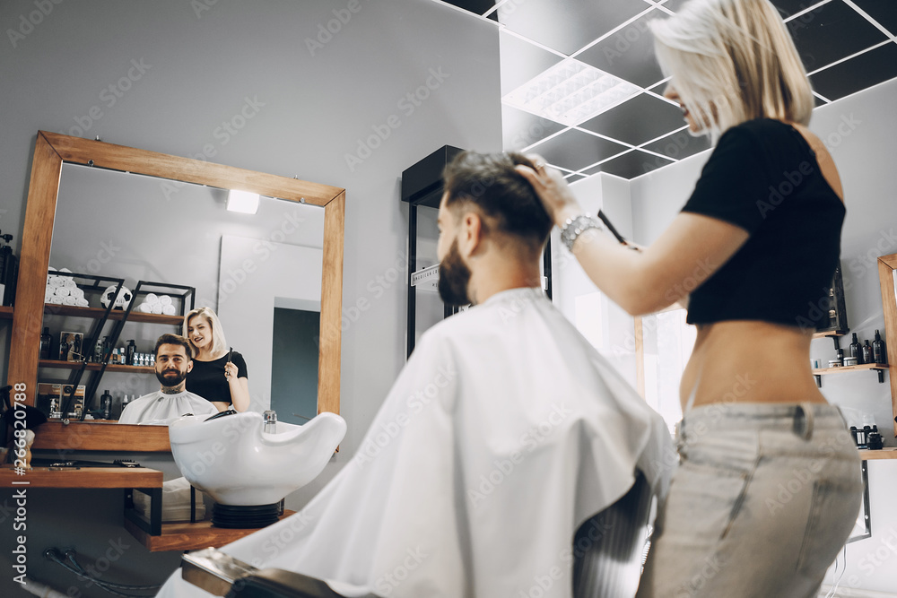 handsome young bearded guy sitting in an armchair in a beauty salon and the girl around him prepares his hair for washing handsome young bearded guy sitting in an armchair in a beauty salon and the girl around him prepares his hair for washing
