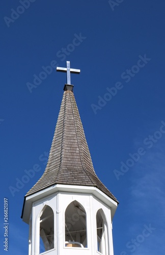 Bell tower and church steeple with stainless steel cross on top isolated on blue sky