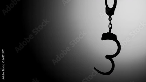 OPEN HANDCUFFS HANGING IN SILHOUETTE, WITH NEGATIVE SPACE.  IN 4K.