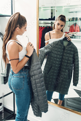 Young woman in a blu jeance white t-shirt trying on gray down coat in a luxury boutique © Mykola