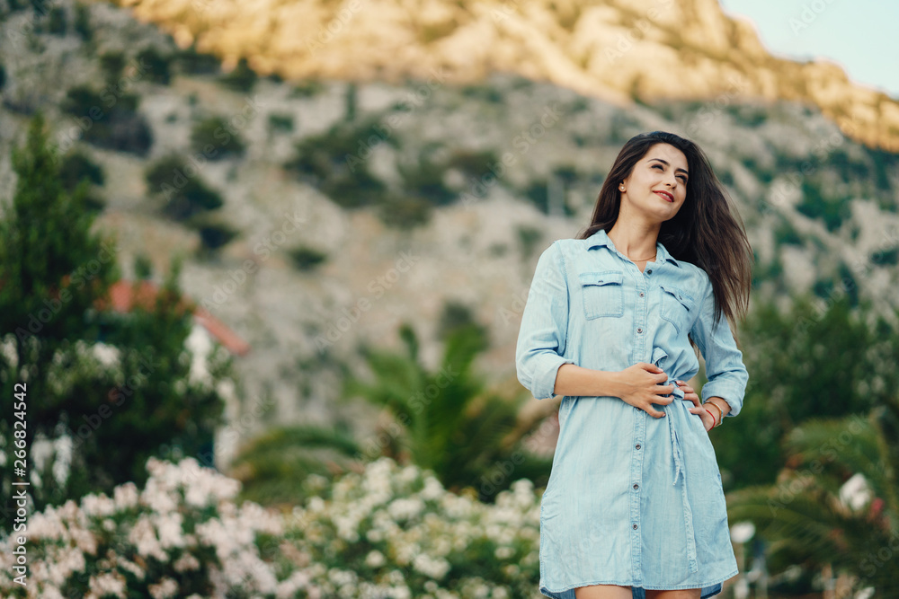 A beautiful young girl in a blue dress standing near the flower tree A beautiful young girl in a blue dress standing near the flower tree