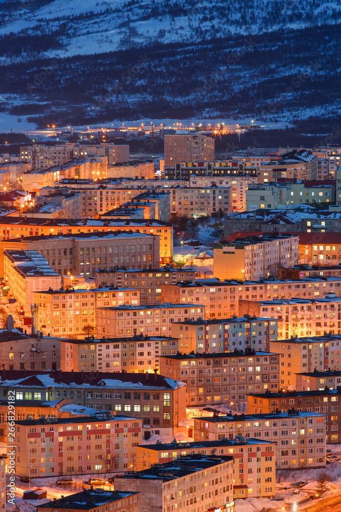 Night cityscape with many buildings. Top view of the city with bright street lighting at dusk. City of Magadan, Siberia, Far East of Russia.